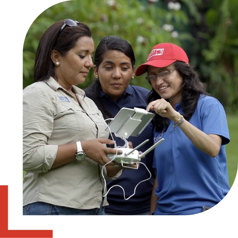 Two women gathered around a third who is holding a drone remote controller.